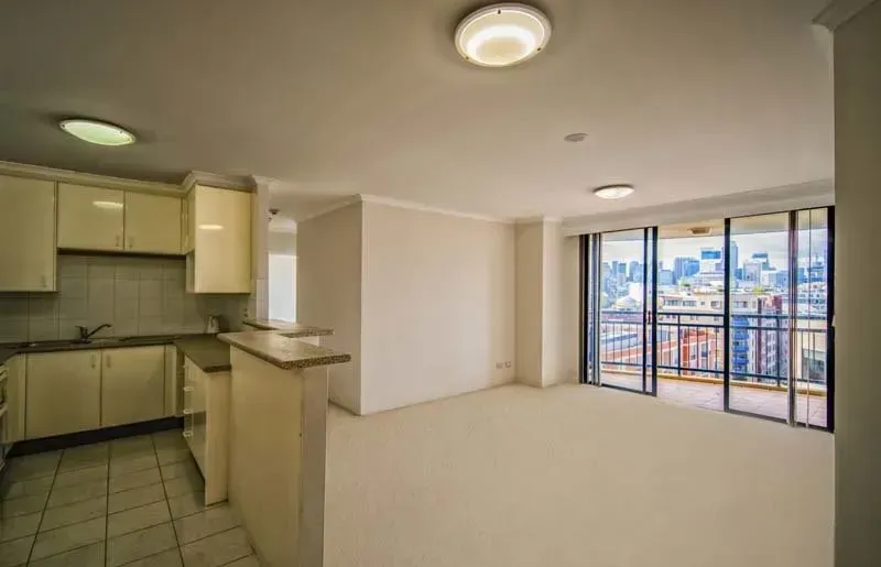 Empty apartment interior with kitchen, living area, and city view balcony.