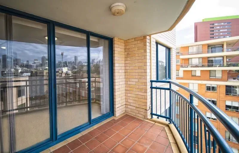 Balcony with city view, blue-framed sliding glass doors, brick walls, and curved metal railing.