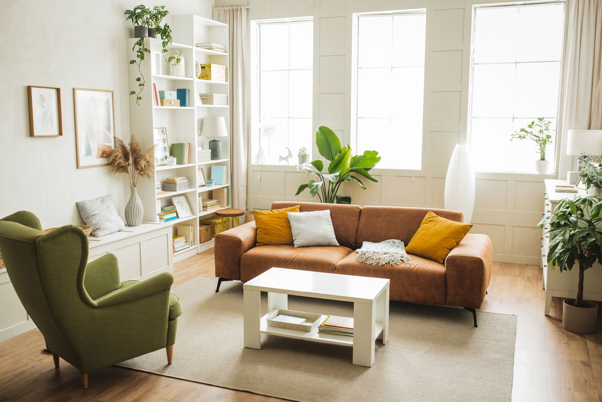 Cozy living room with brown sofa, olive green armchair, white bookcase, and large windows.