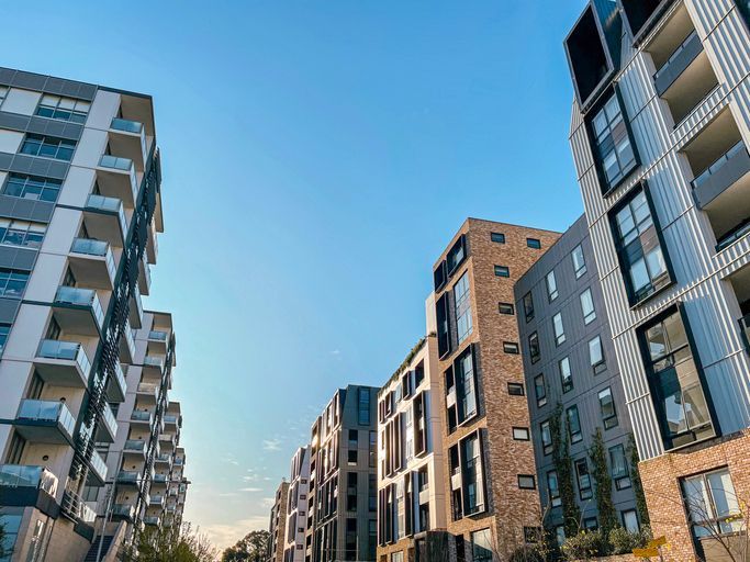 Hand holding keys with house-shaped keychains in front of a yellow house, sunny outdoor setting.