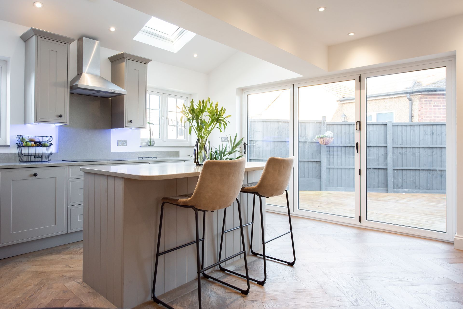 Spacious gray kitchen with island and two bar stools. Large sliding glass doors lead to a backyard.