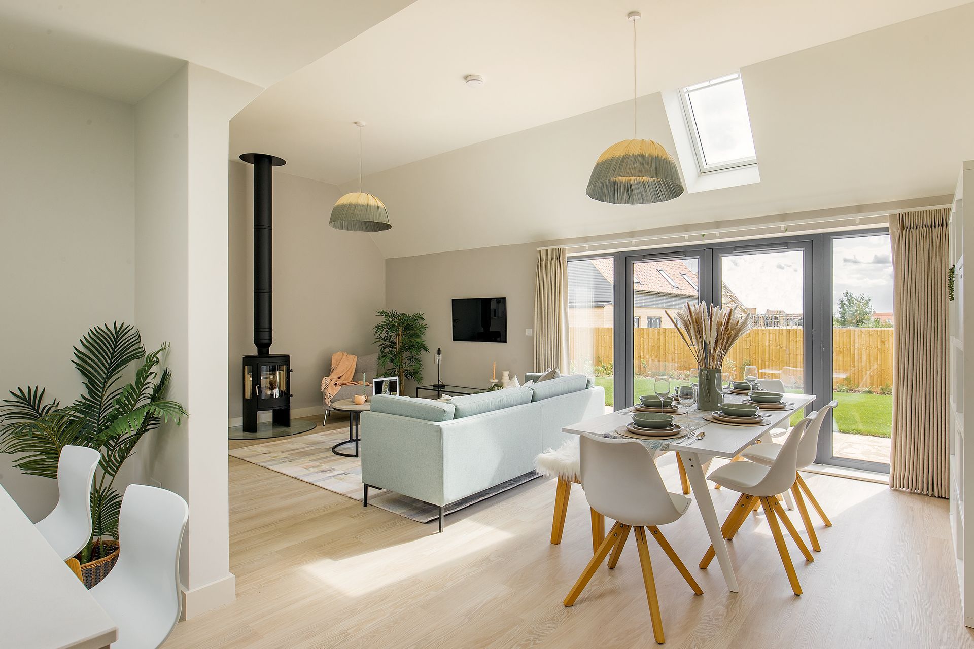 Open-plan living area with dining table, sofa, fireplace, and large windows opening onto a garden.