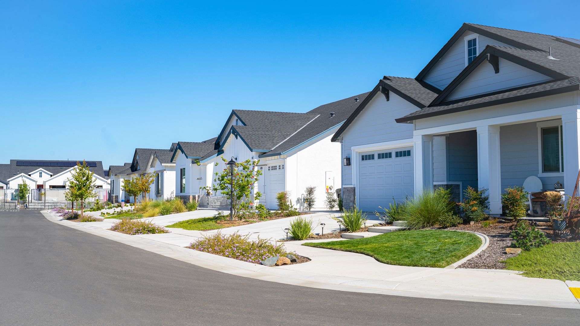 Row of modern homes with gray exteriors, white garages, and manicured lawns on a sunny day.