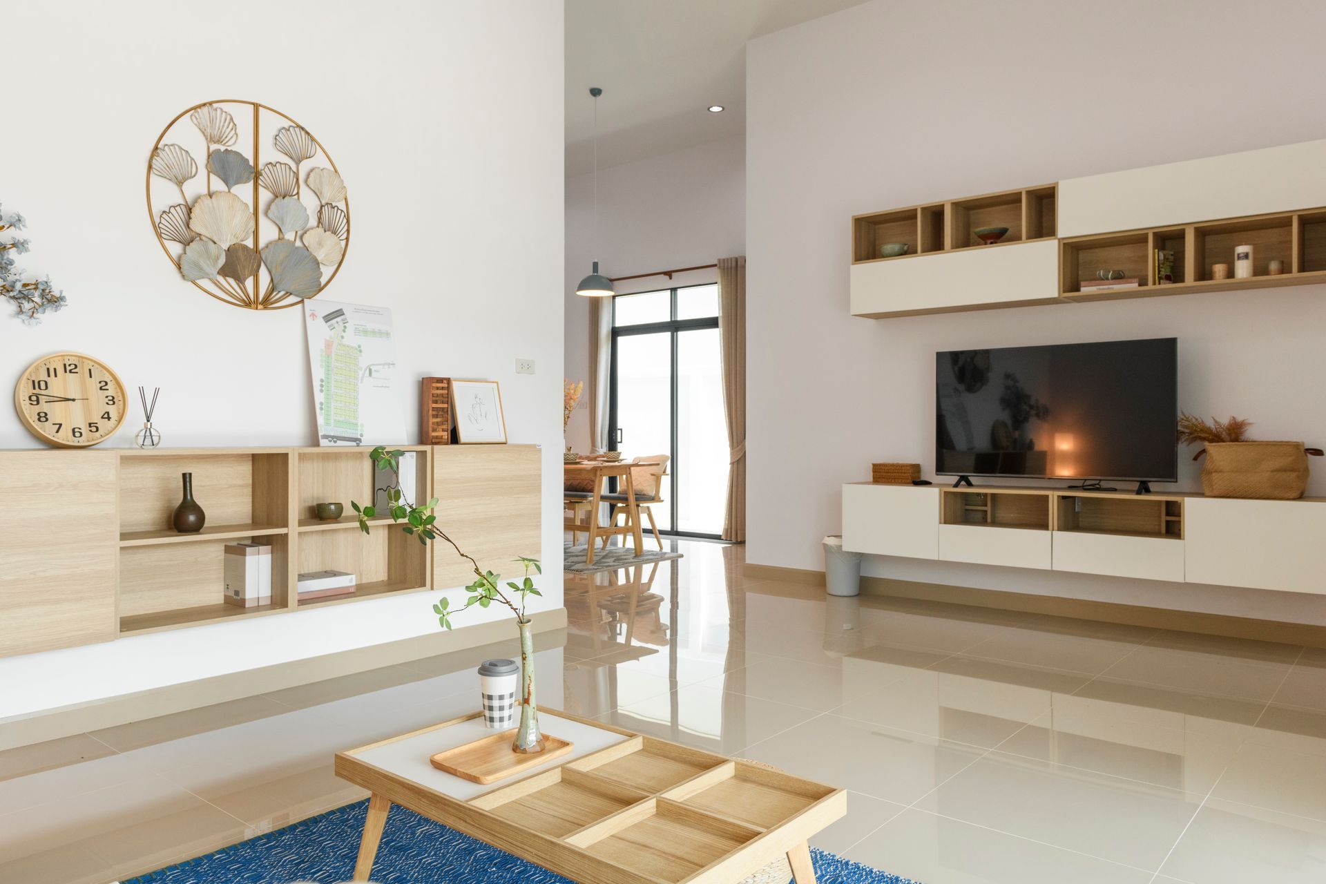 Living room with light wood furniture, a TV, and decorative wall art; neutral color scheme.