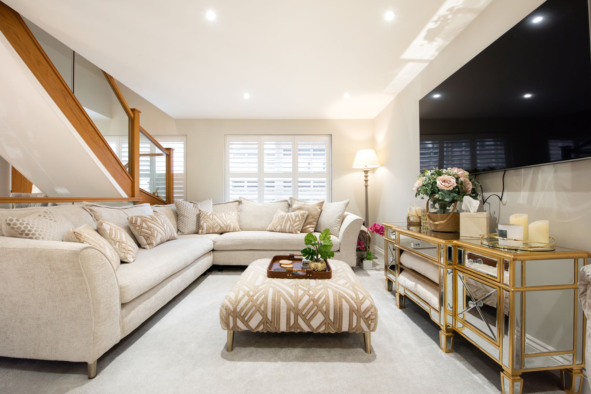 Living room with sectional sofa, ottoman, mirrored side table, and stairs.