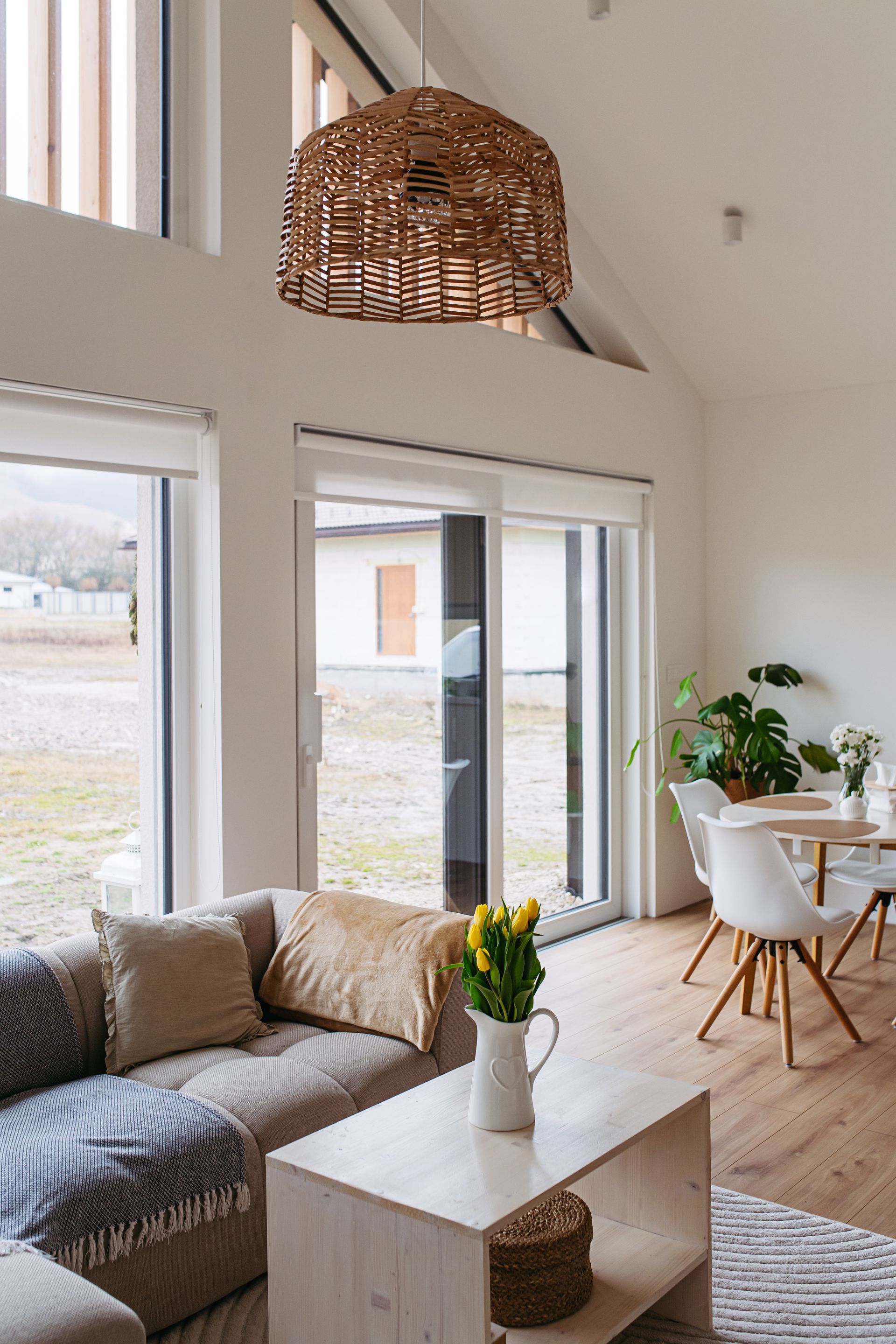 Living room with light wood floors, neutral sofa, woven pendant lamp, and white walls.