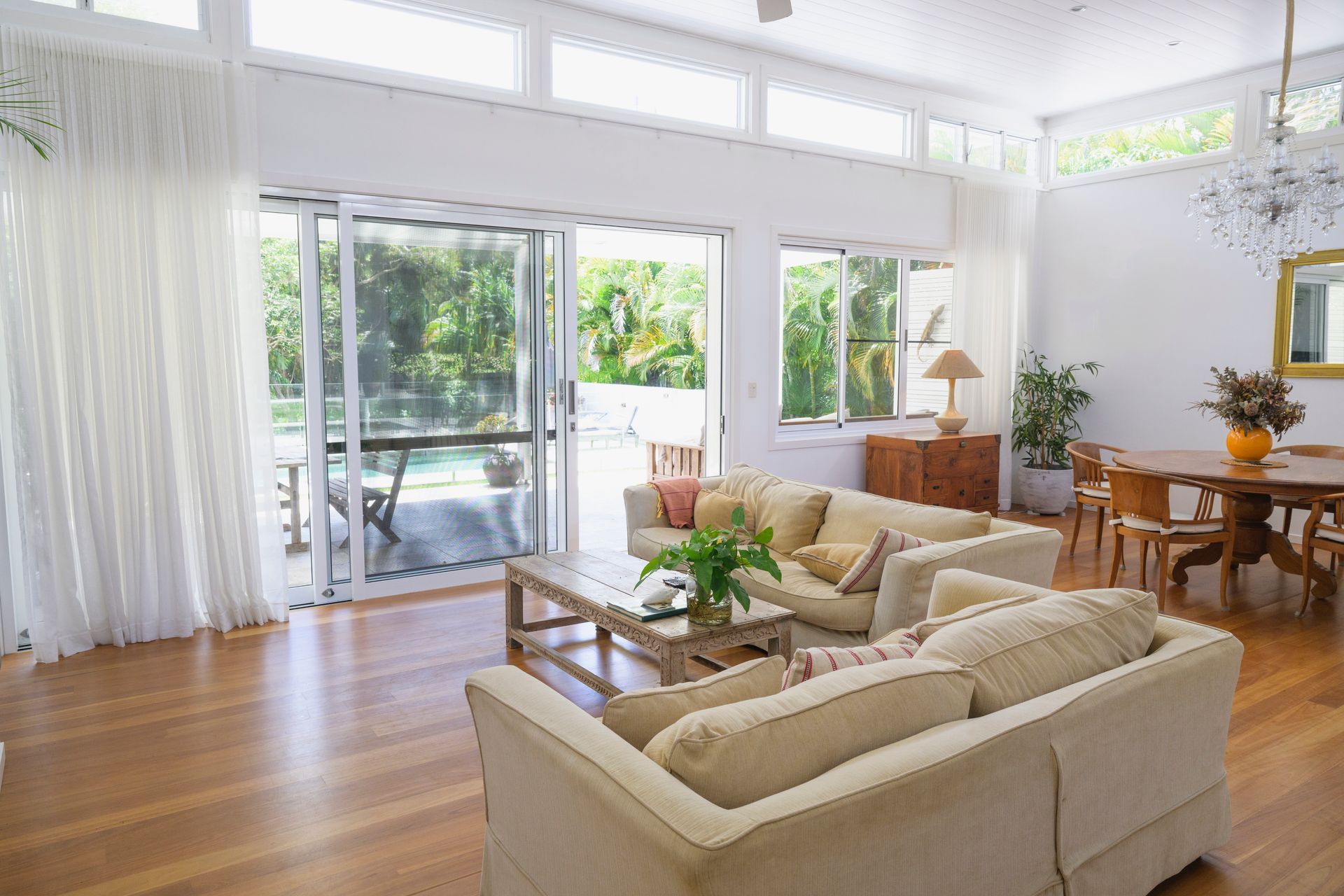 Bright living room with couches, dining table, and sliding glass door to a patio and pool.