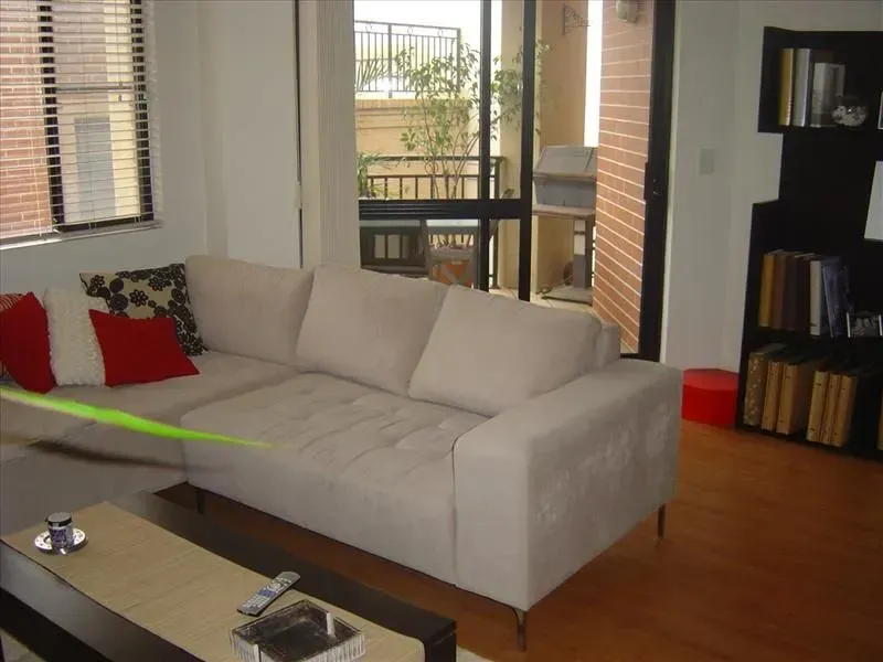 Beige couch in a living room with a window, balcony, and a bookcase.