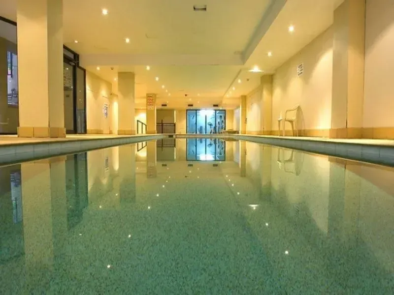 Indoor lap pool with reflecting water, beige walls, and bright overhead lights.