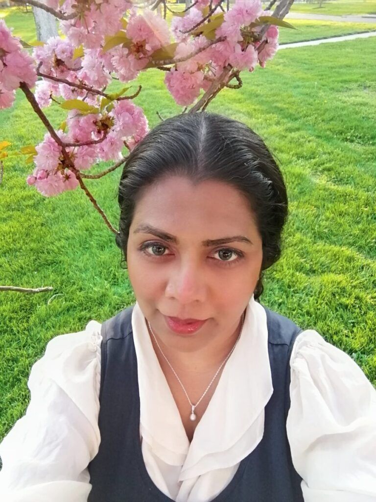 Woman taking a selfie under pink blossoms in a green park