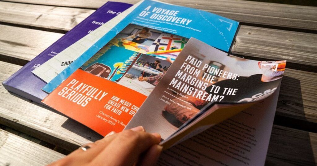 Hand holding a stack of colorful brochures on a wooden table, one leaflet open in front