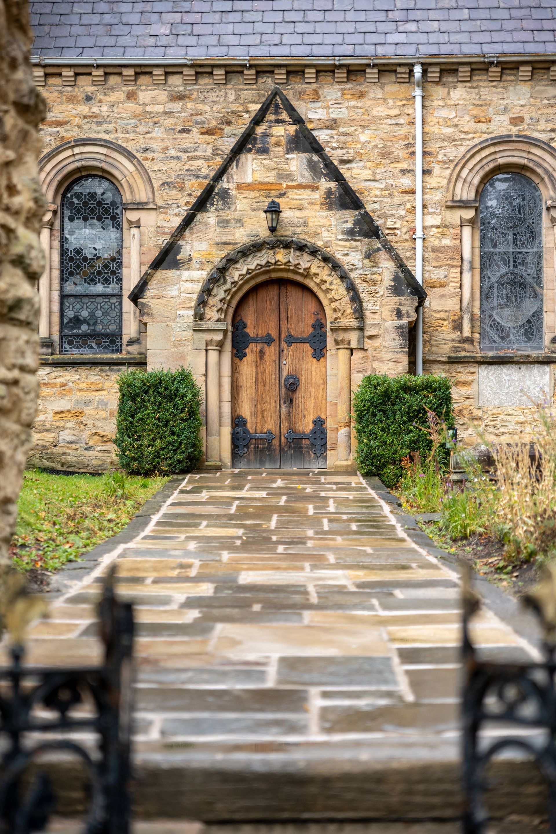 Stone church entrance with arched wooden door, stained-glass windows, and a flagstone path