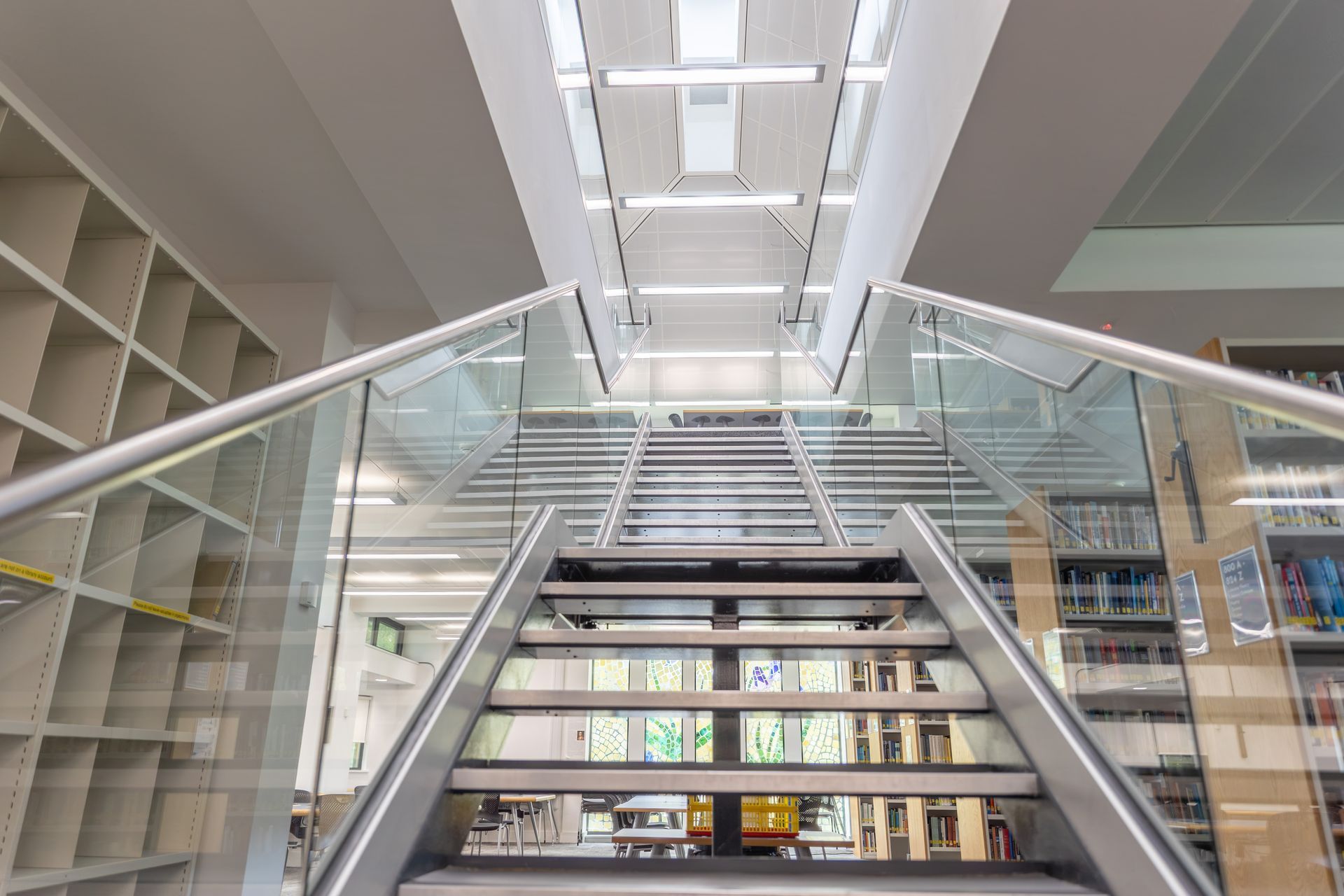 Modern library interior with a central staircase and glass railings between tall bookshelves