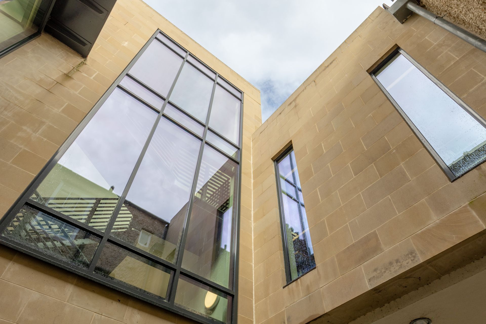 Modern building courtyard with tall beige walls and large reflective windows viewed upward