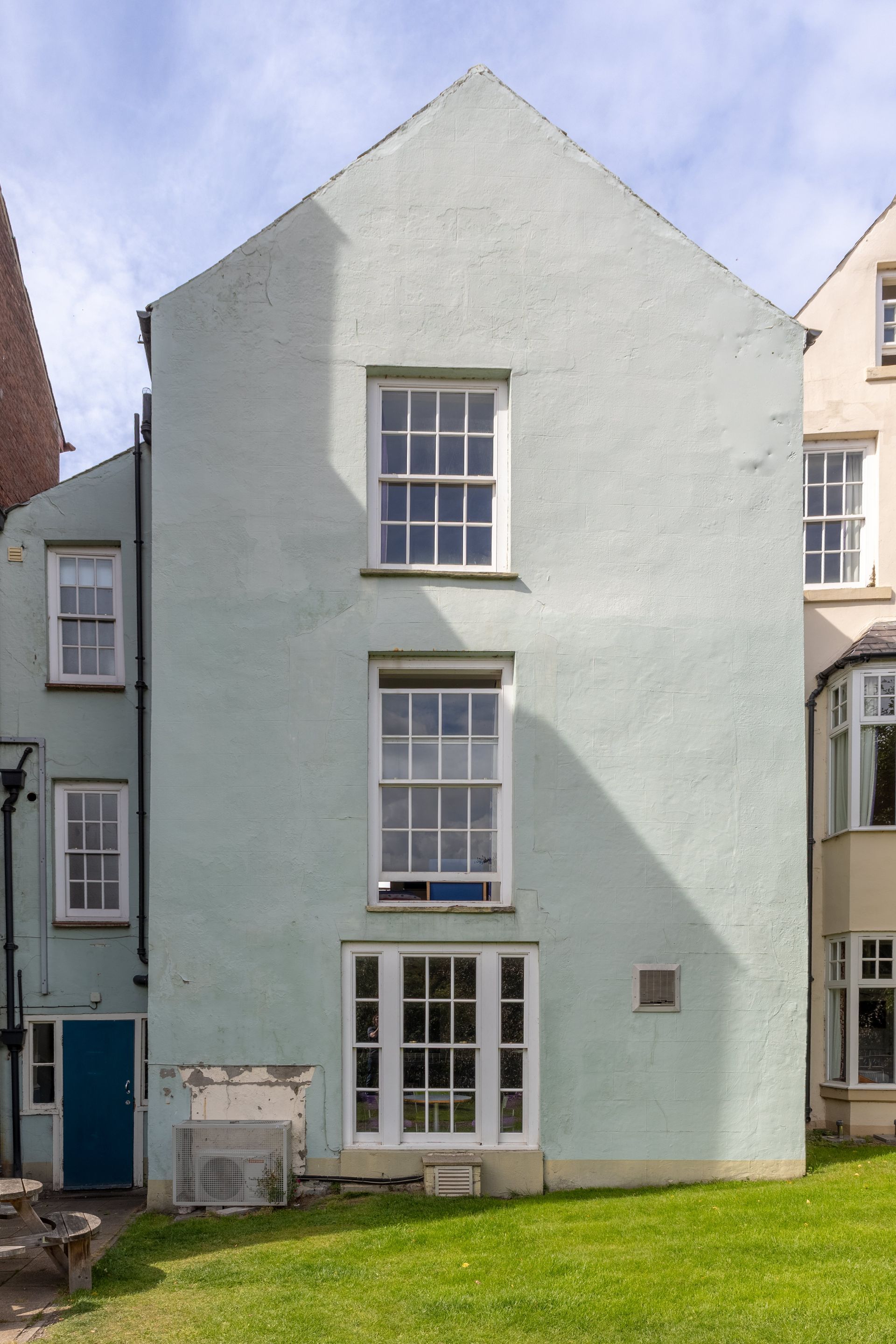 Pale green three-story house facade with white-trimmed windows and a small grassy front yard.