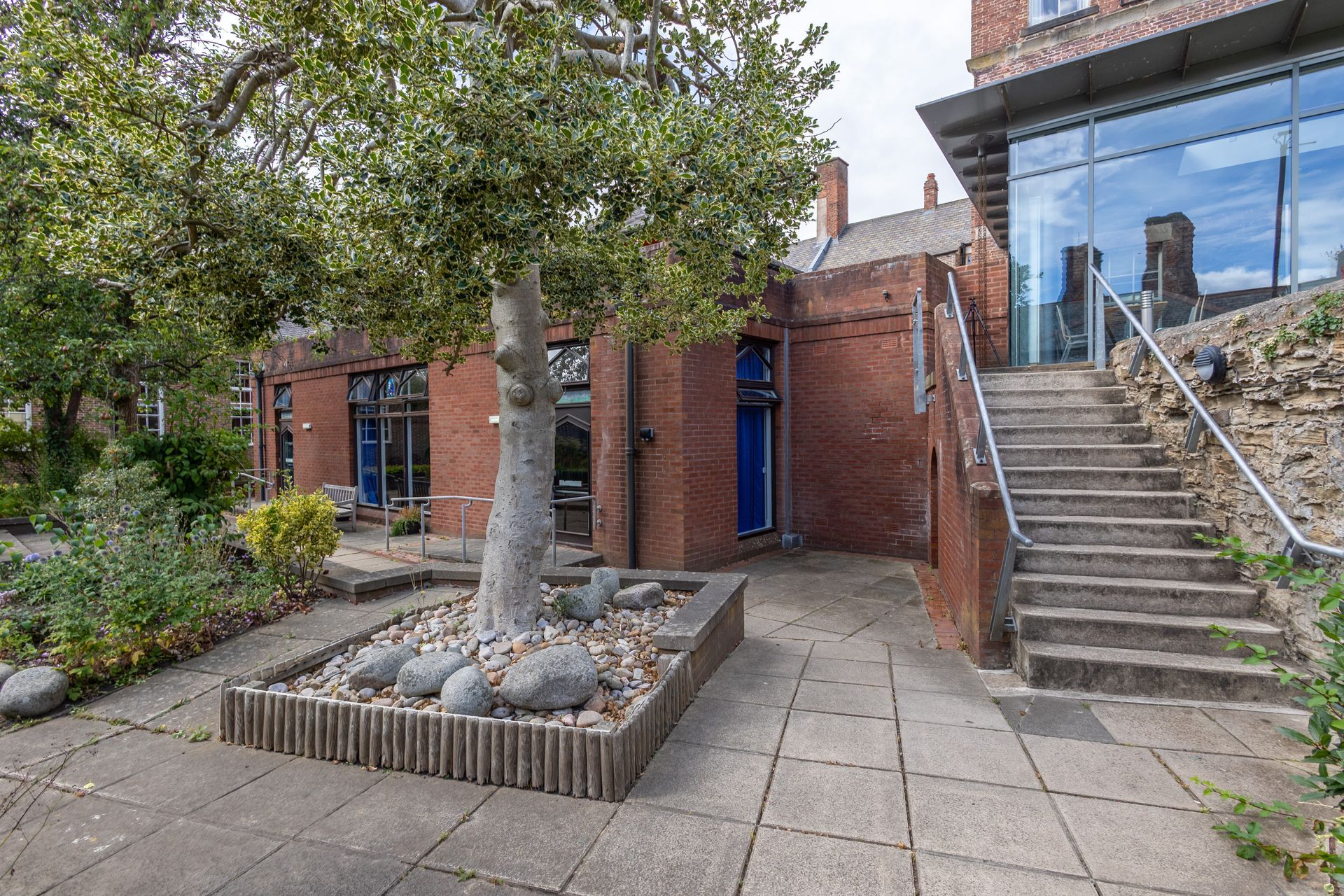 Brick courtyard with a tree planter, paved path, and stairs beside a brick building