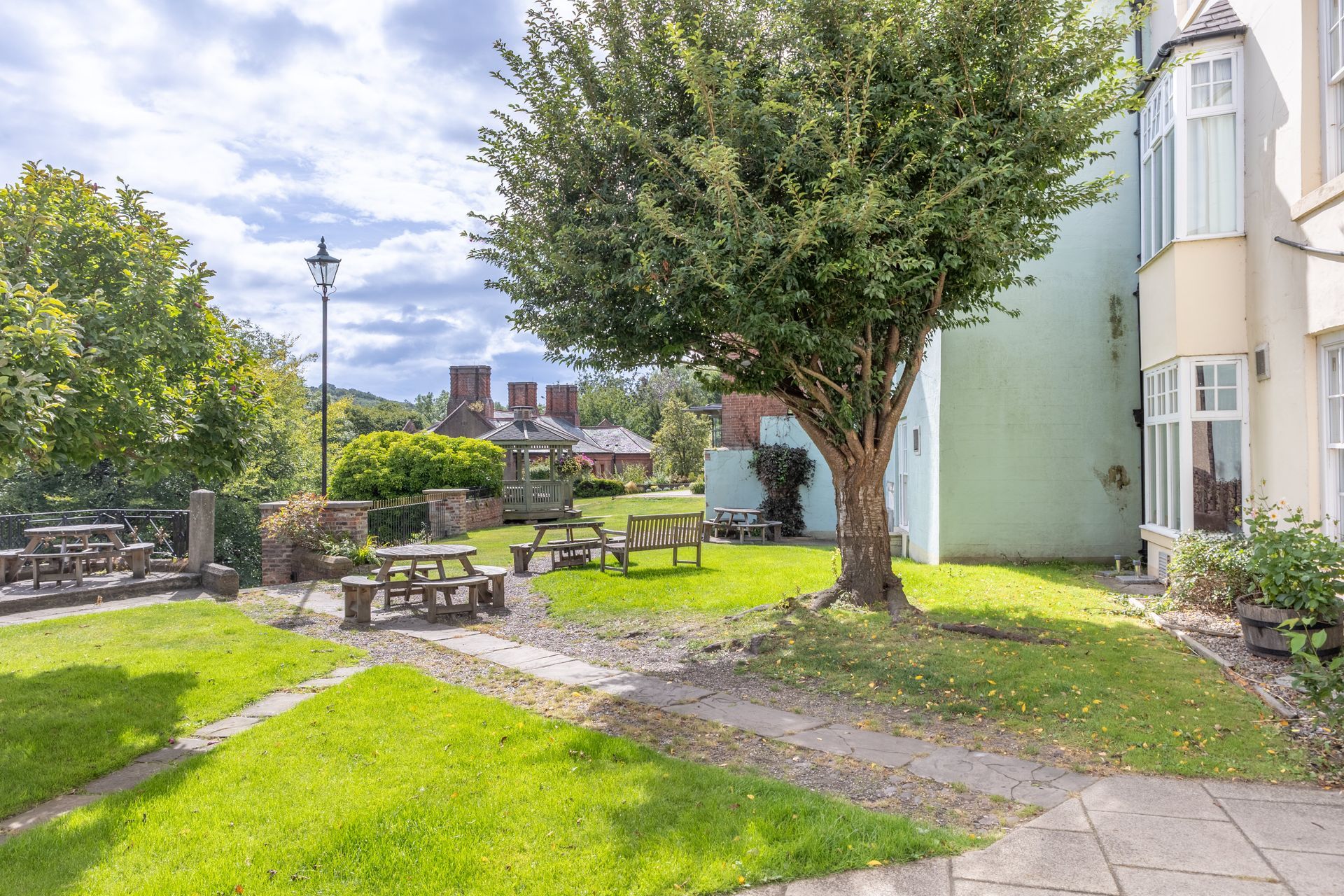 Courtyard garden with picnic tables, green grass, a large tree, and a building beside a paved path