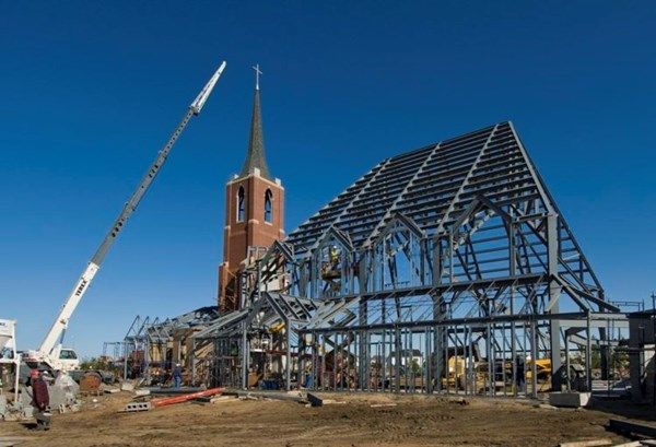 Construction site with a steel-frame building, church tower, and crane under a clear blue sky