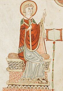 Medieval illustration of a haloed seated saint in red and white robes, holding a staff beside a decorated book stand