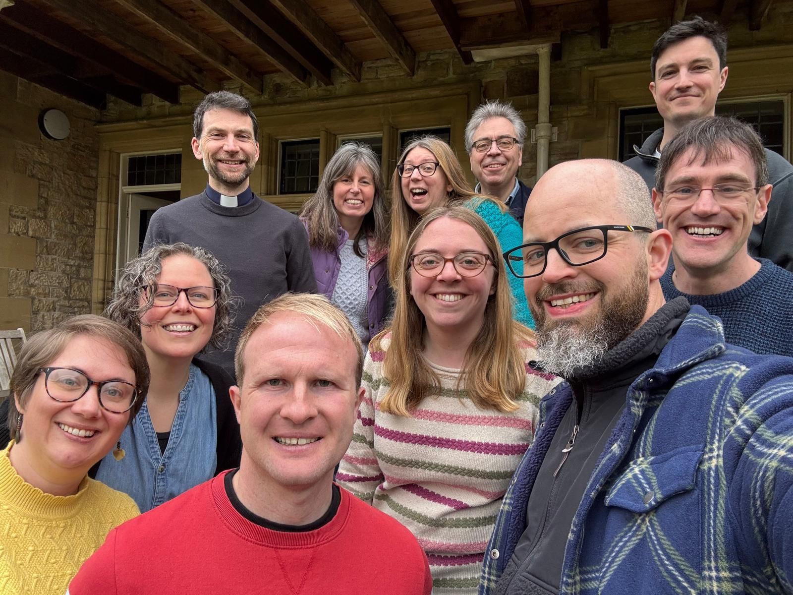 Group selfie of ten smiling people on a rustic wooden porch, with trees visible in the background.