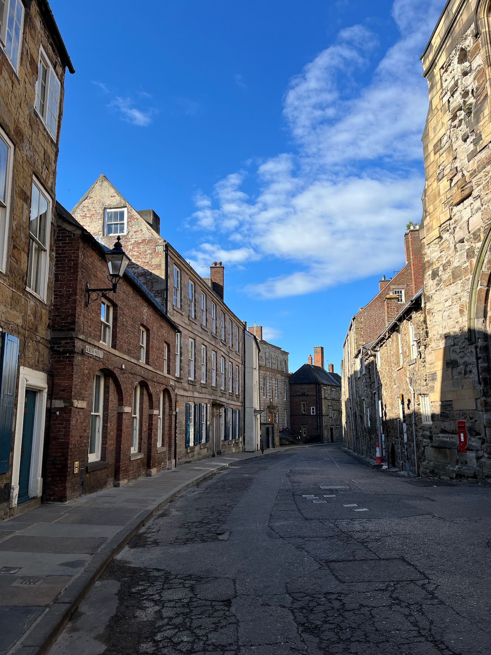 Narrow cobblestone street lined with old brick and stone buildings under a blue sky
