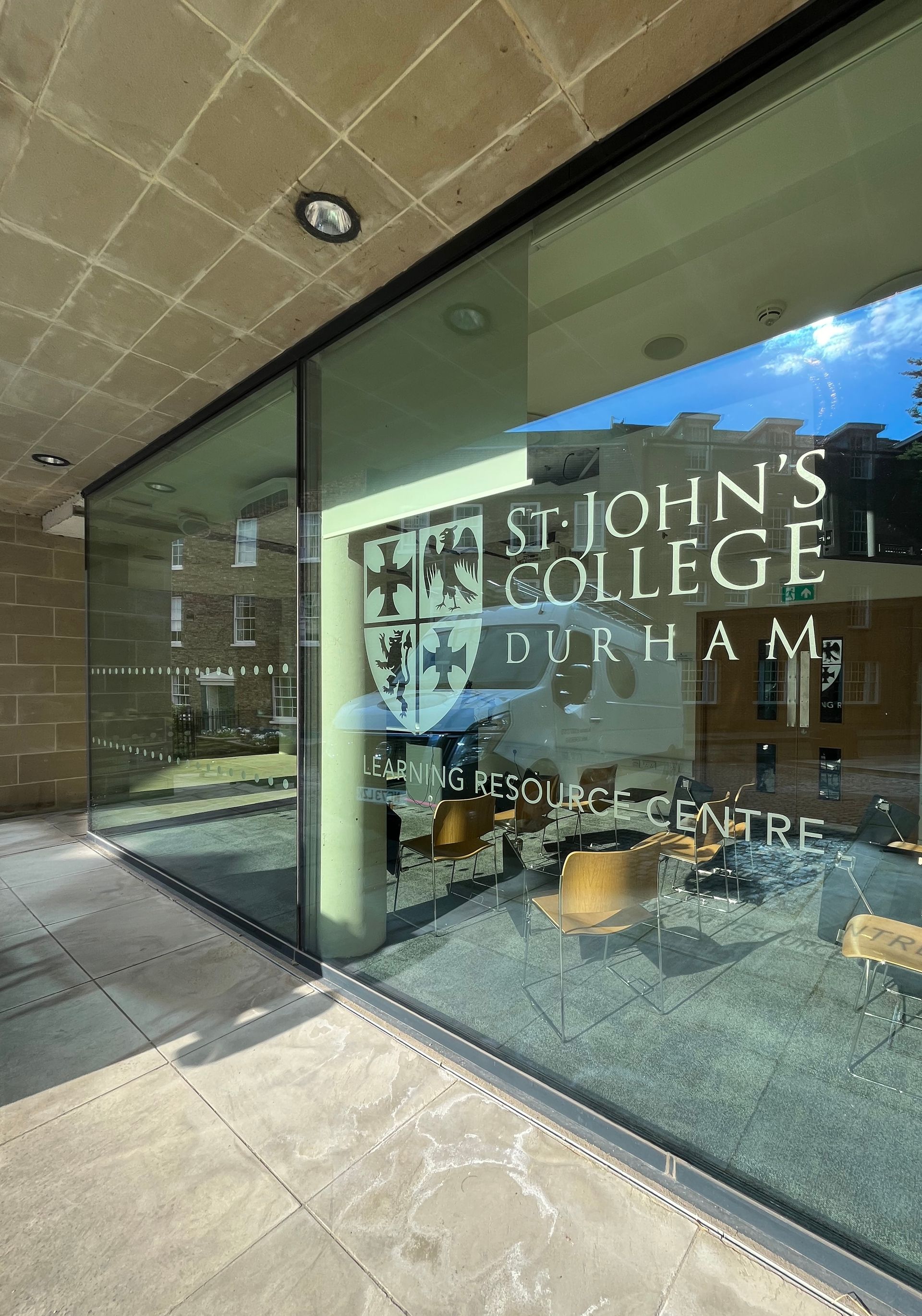 Exterior of St. John's College building with glass entrance and reflected sky.