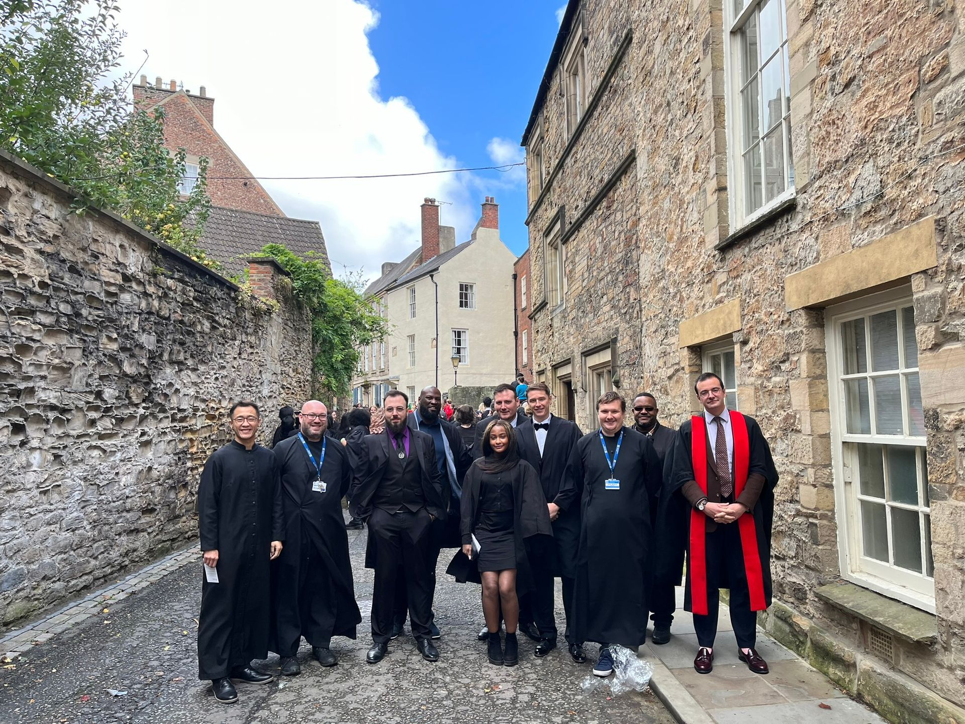 Group of people in black robes standing in a narrow stone alley beside old buildings