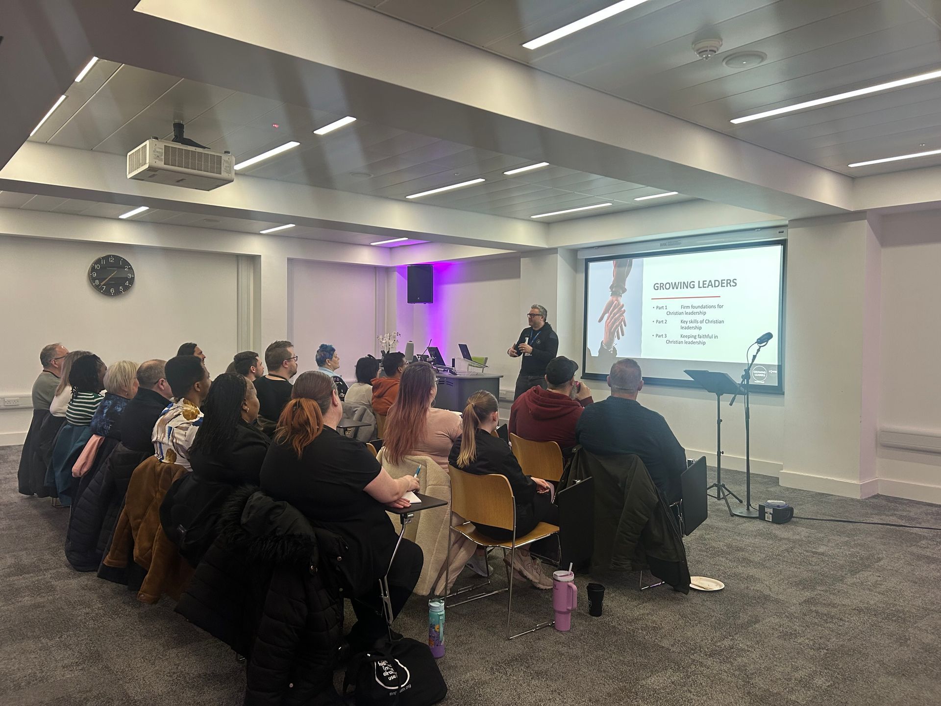 Audience seated in a conference room watching a speaker present slides on a screen
