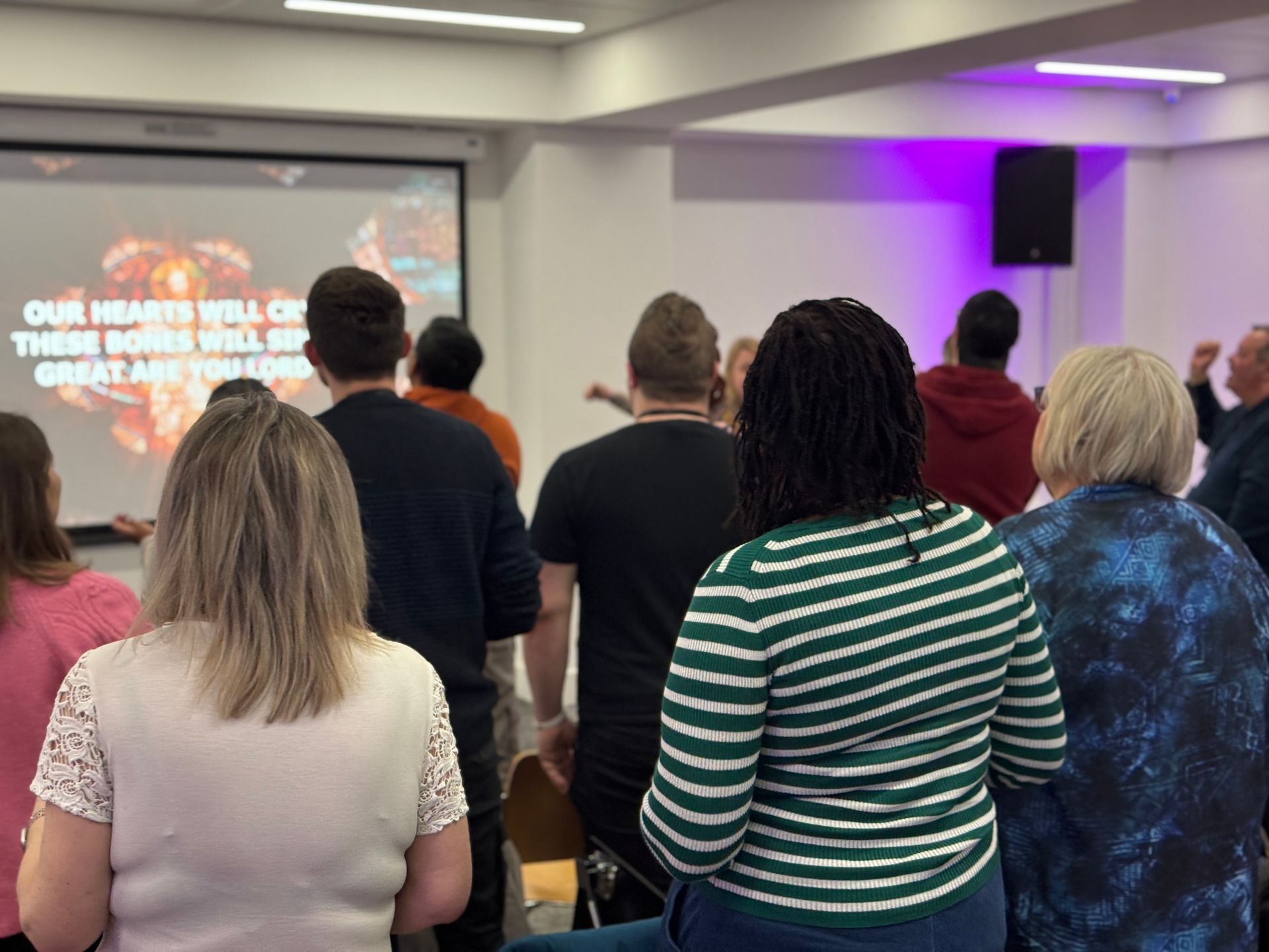 People standing in a room facing a projected presentation screen during a talk.