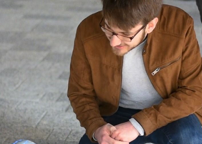 Man in a brown jacket sitting and looking down on a concrete floor