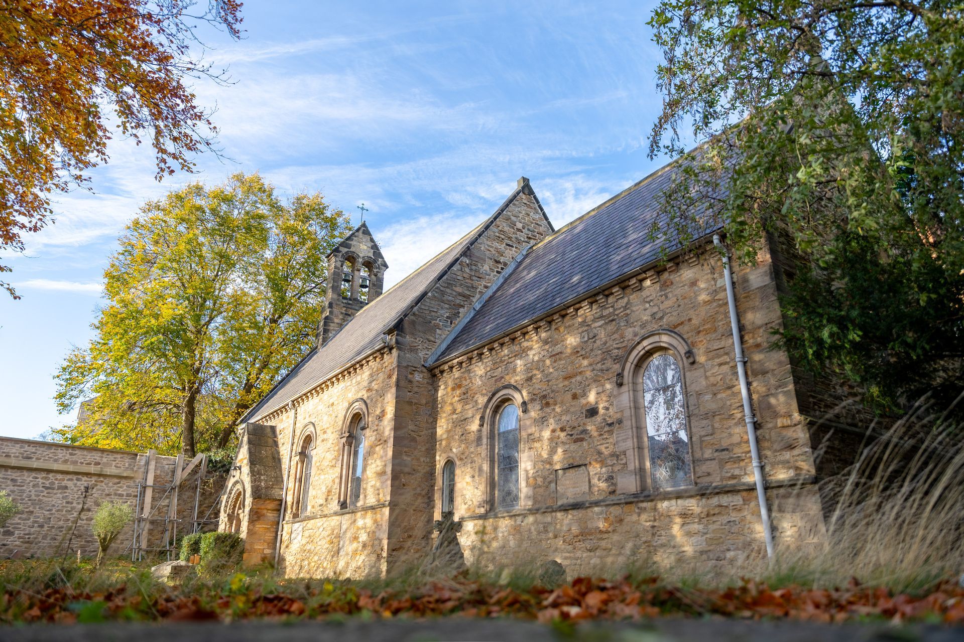 Stone church with arched windows beside a wall, lit by warm autumn sunlight under a blue sky