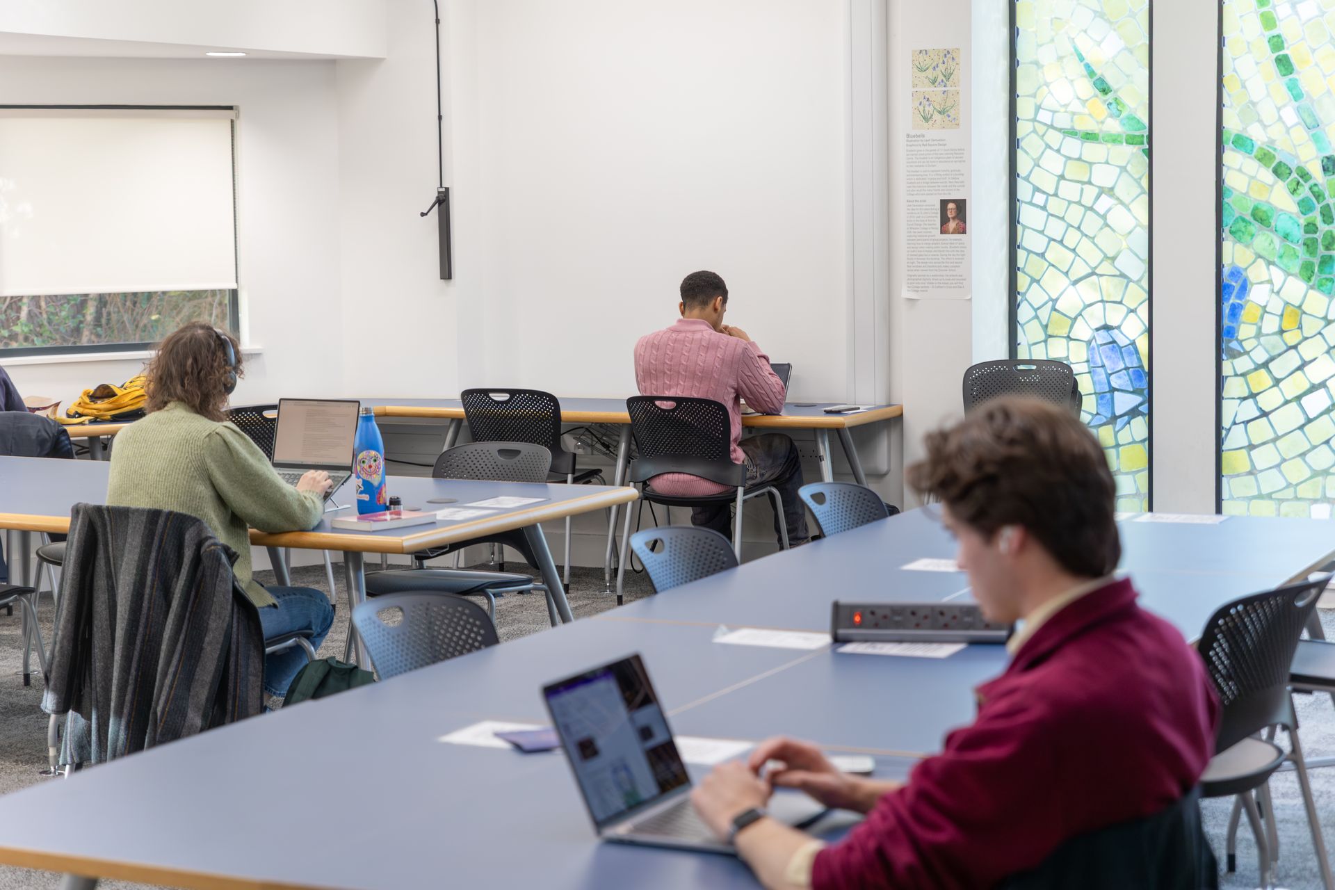 People seated at tables in a bright study room, with laptops and papers.