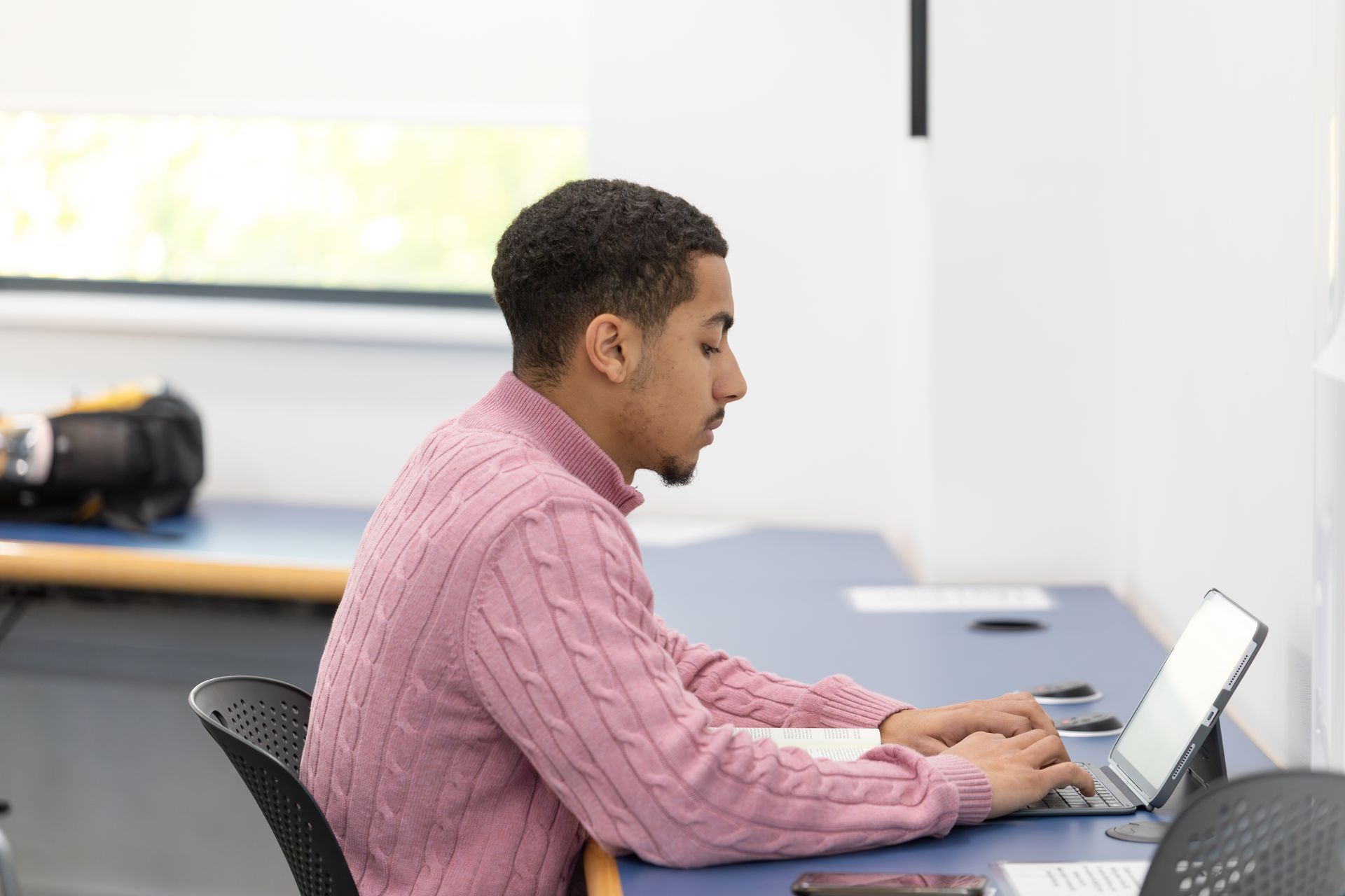 Man typing on a laptop at a desk in a bright office