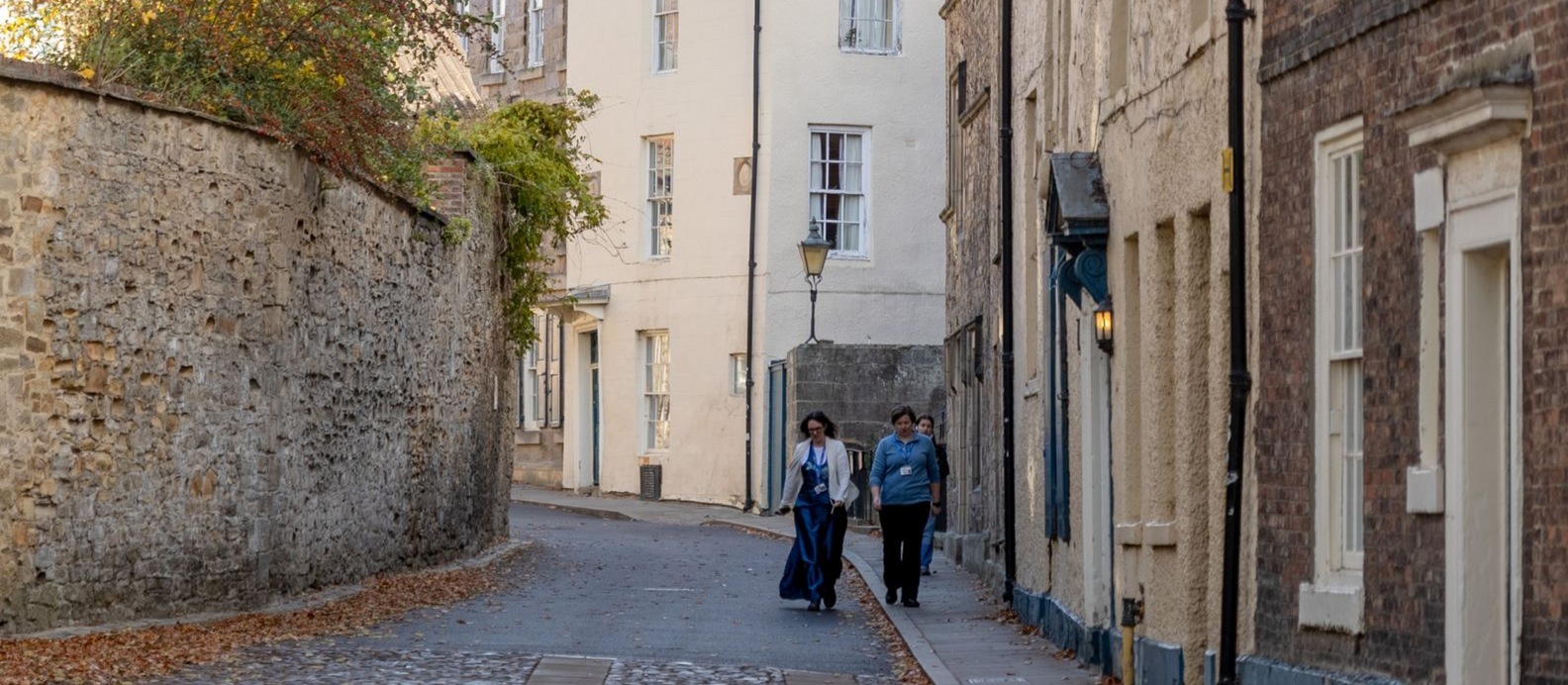 Two people walking a narrow cobblestone street between old stone buildings