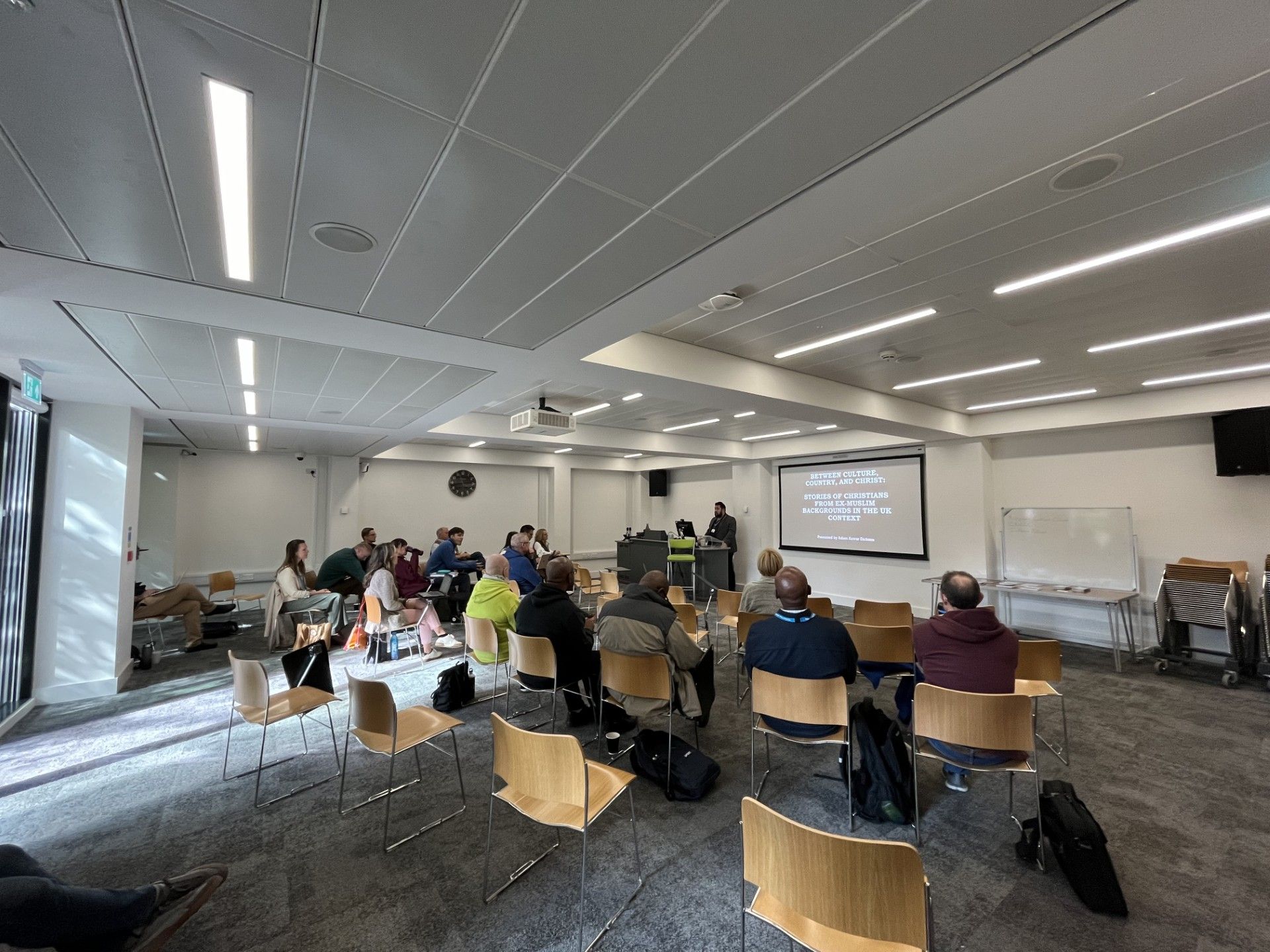 People seated in a meeting room facing a projected presentation screen.