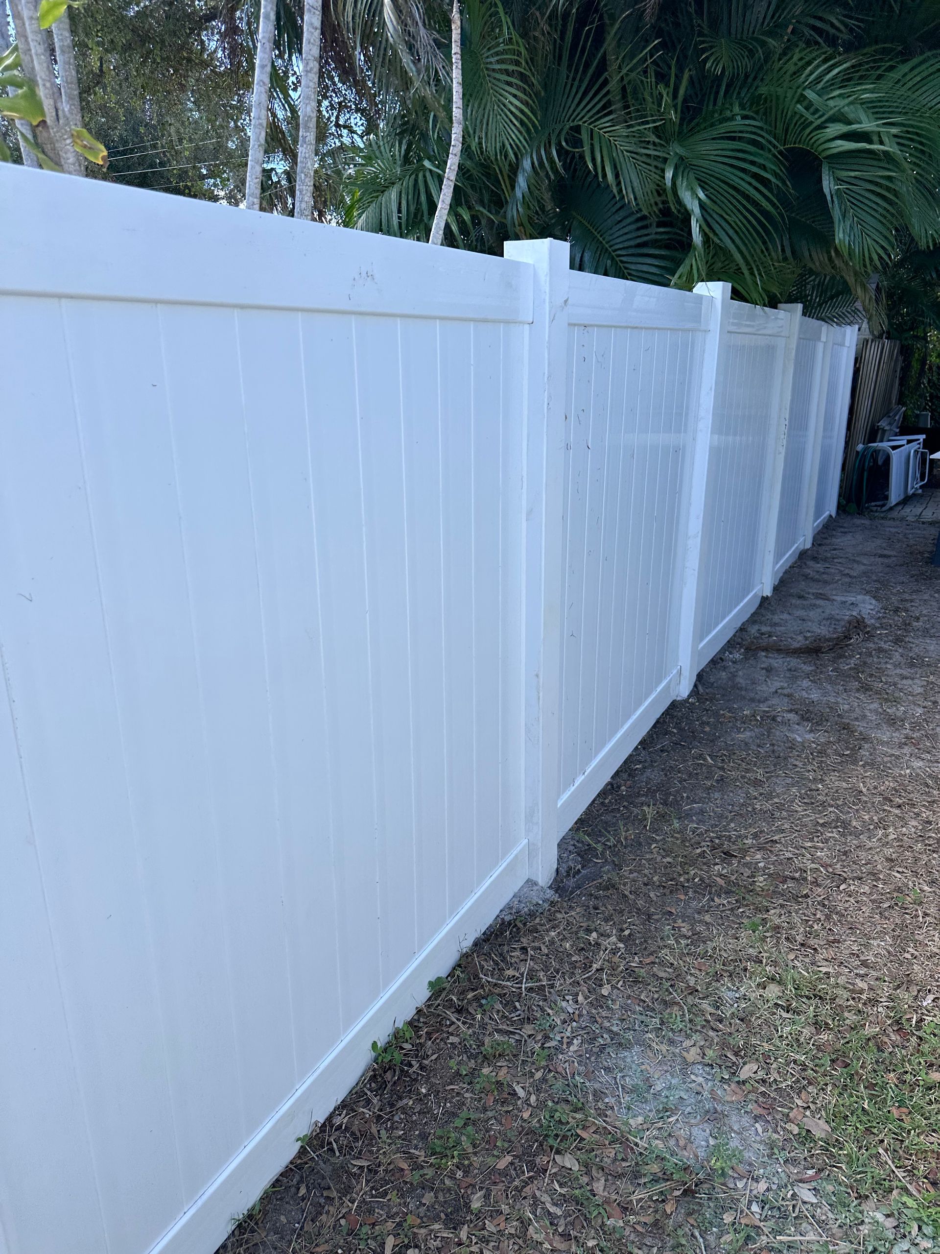 White vinyl privacy fence in a yard with trees and grass.