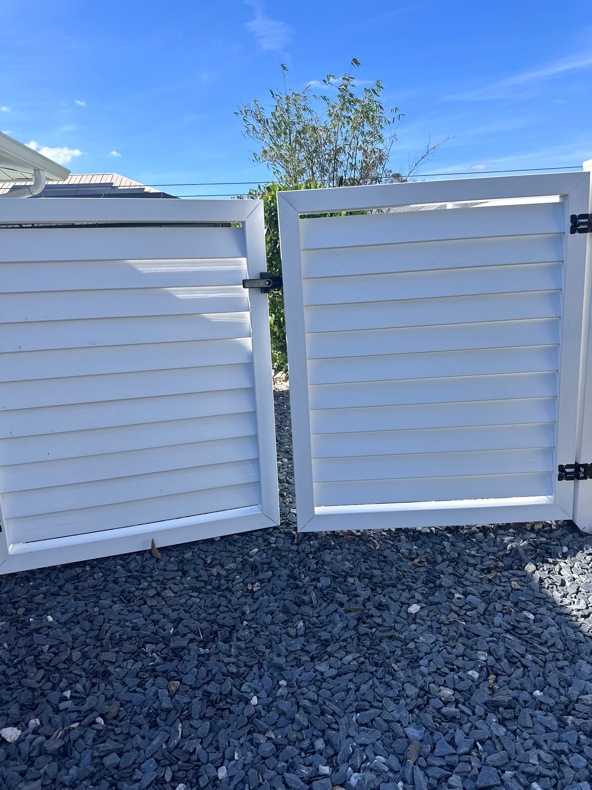 White wooden gate, one side open, on gravel. Blue sky background.