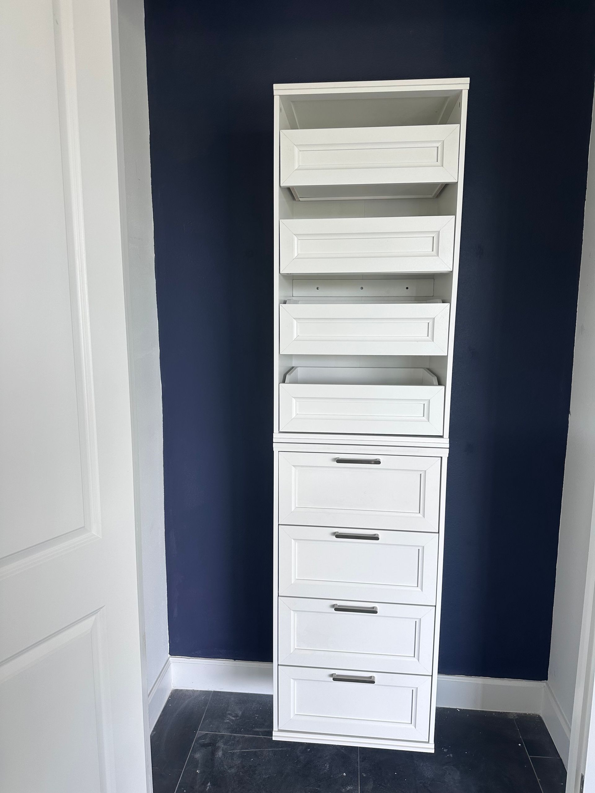 White closet organizer with drawers and shelves against a blue wall in a room.