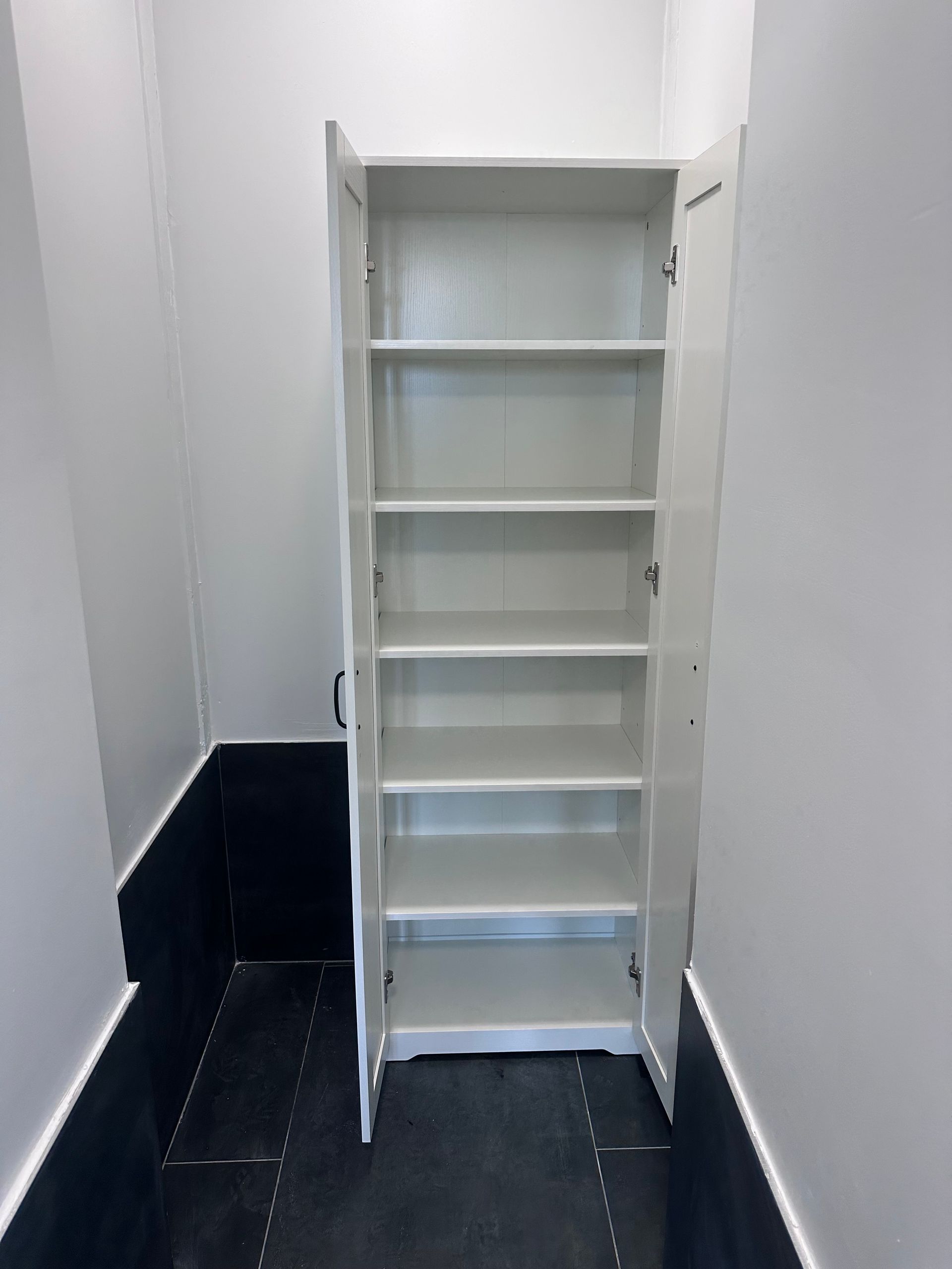 White cabinet with open doors and shelves in a narrow hallway.
