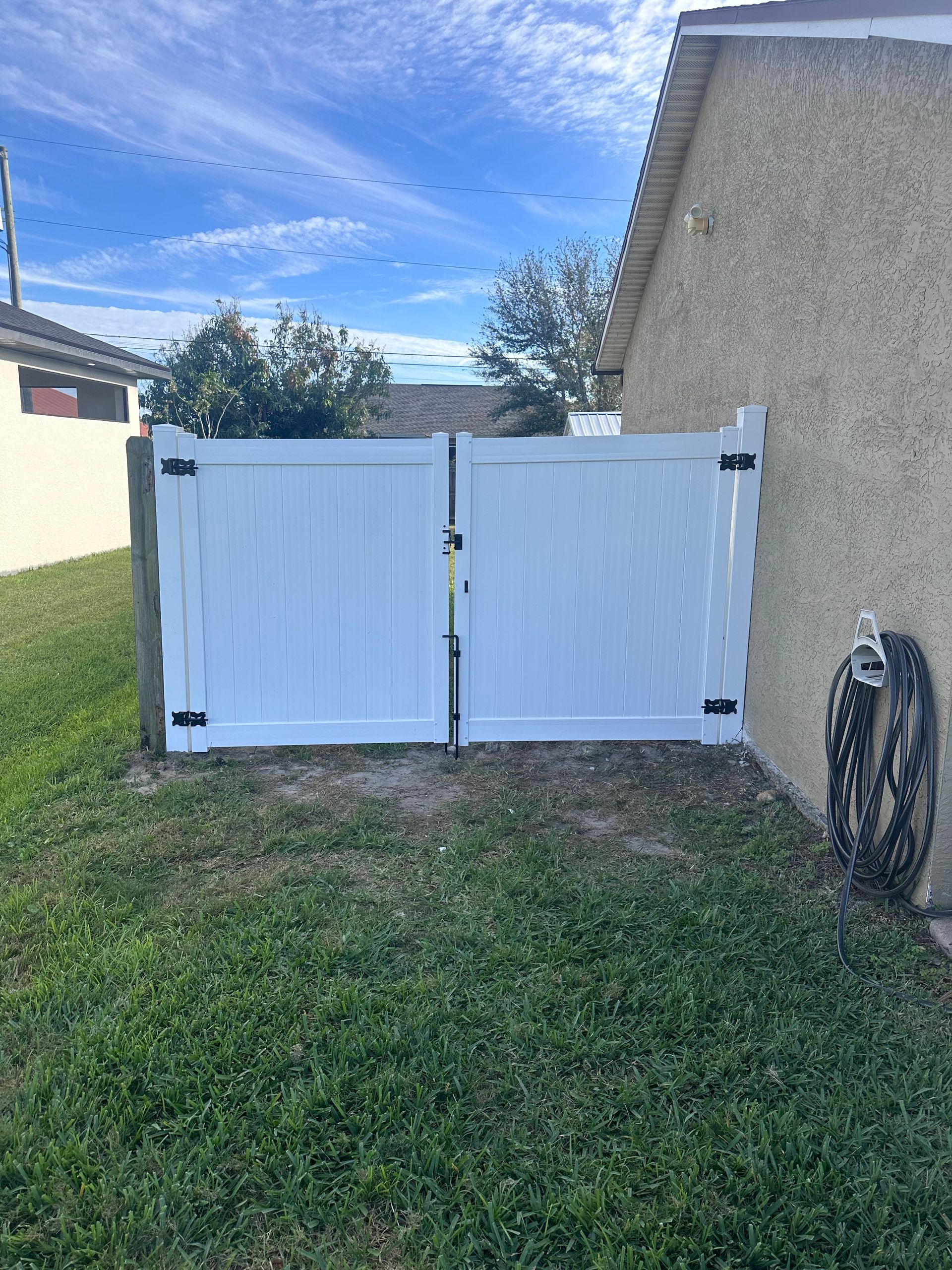 White vinyl gate in a grassy yard, attached to a beige house.