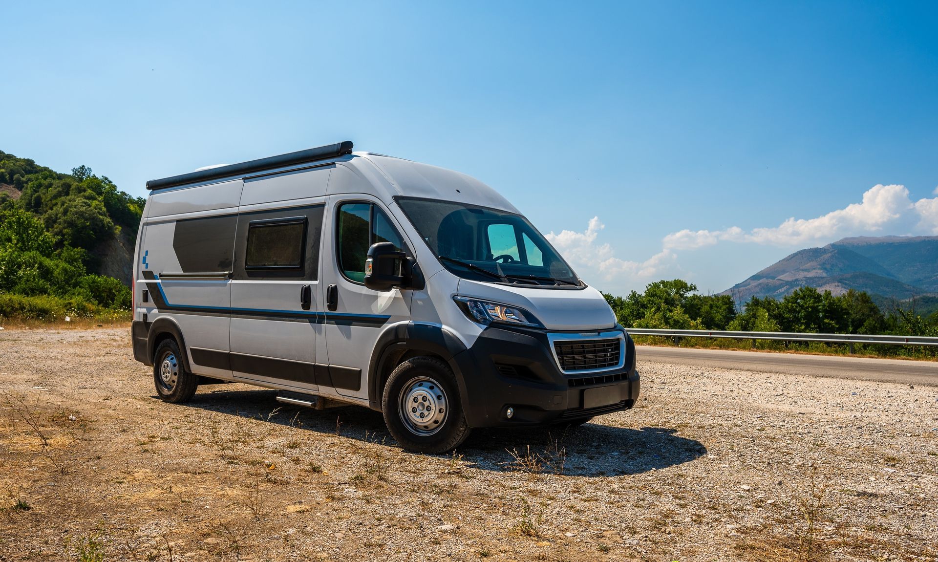 White campervan parked on gravel road with mountains in the background under a blue sky.