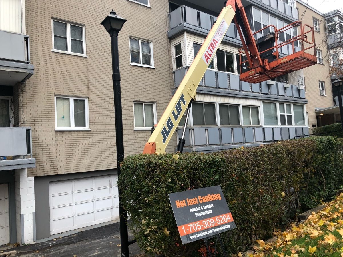 A cherry picker next to a beige apartment building; a sign for 