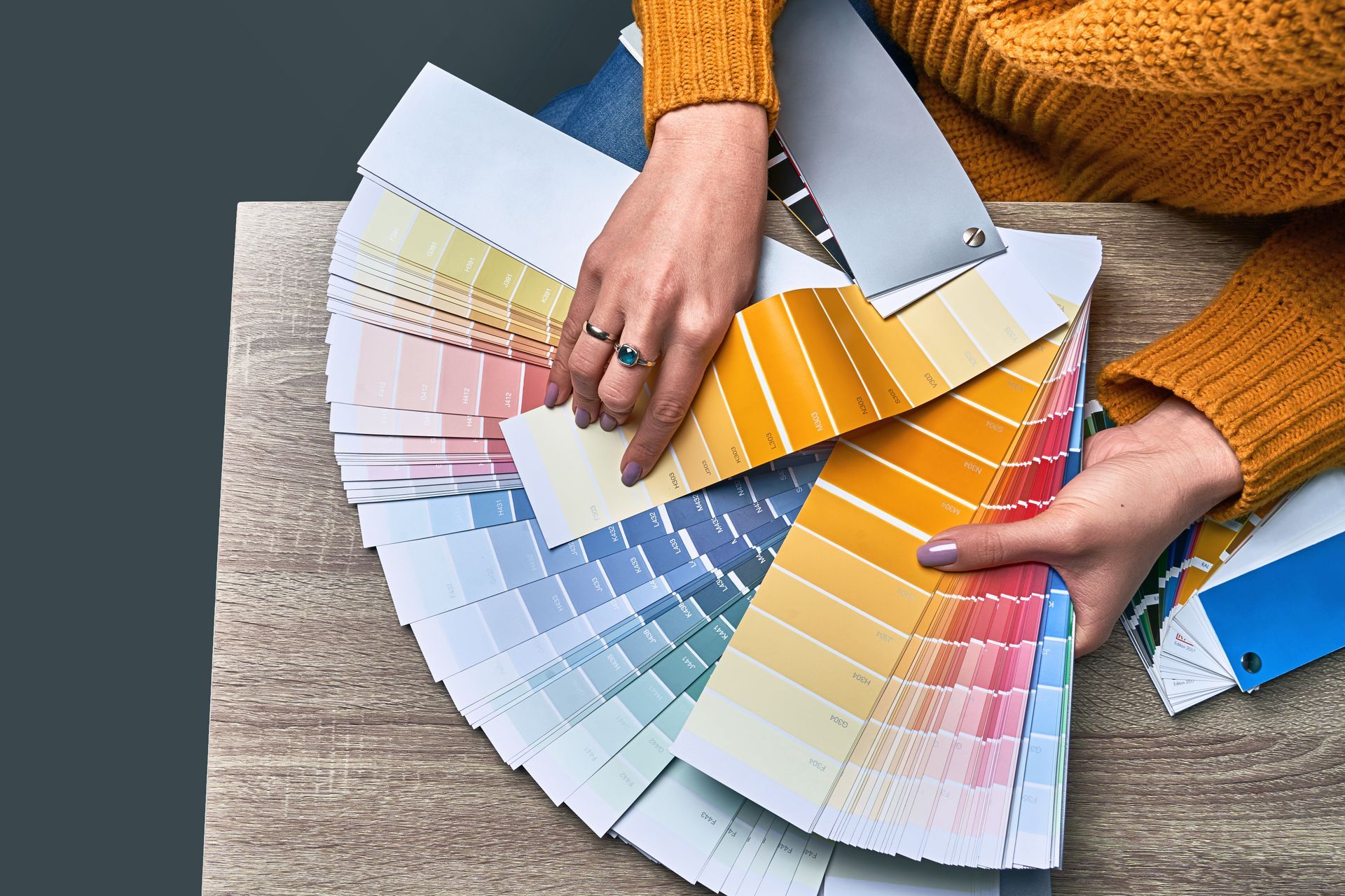 Person holding a fan of paint swatches, selecting colors, indoors.