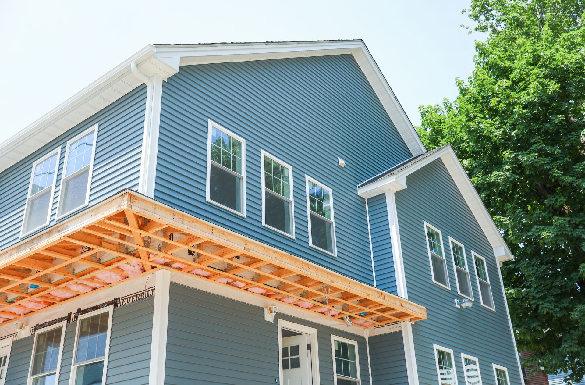 A blue house with a wooden porch is under construction.