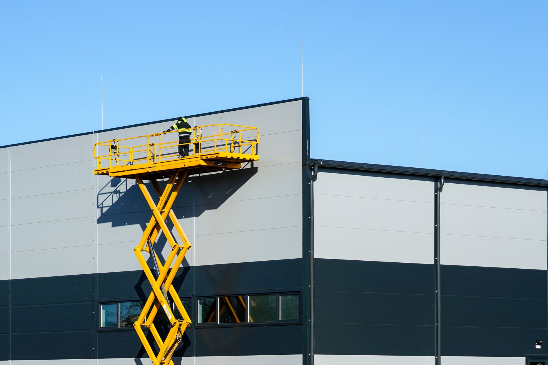 A man is standing on a scissor lift on the side of a building.