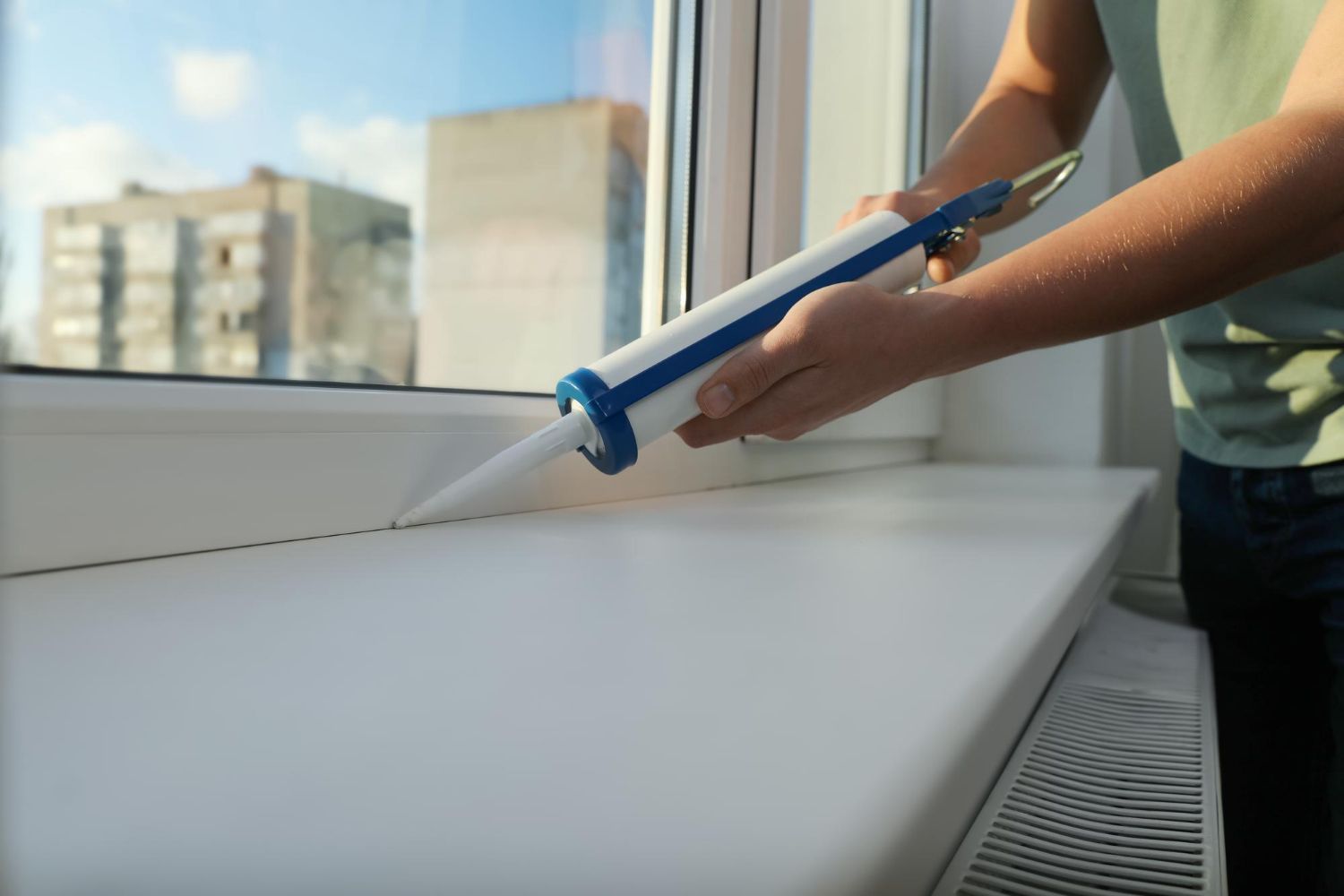 A person is applying caulk to a window sill.