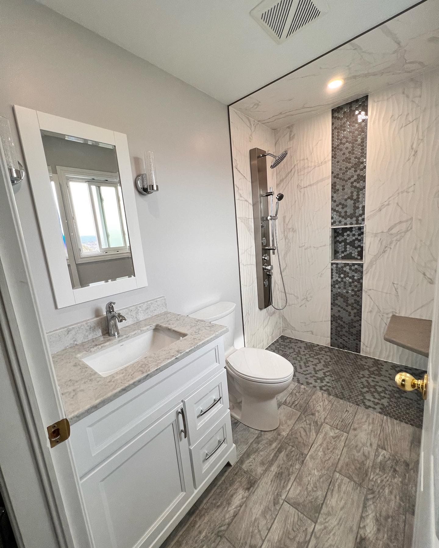 A bathroom with a toilet , sink , mirror and walk in shower.