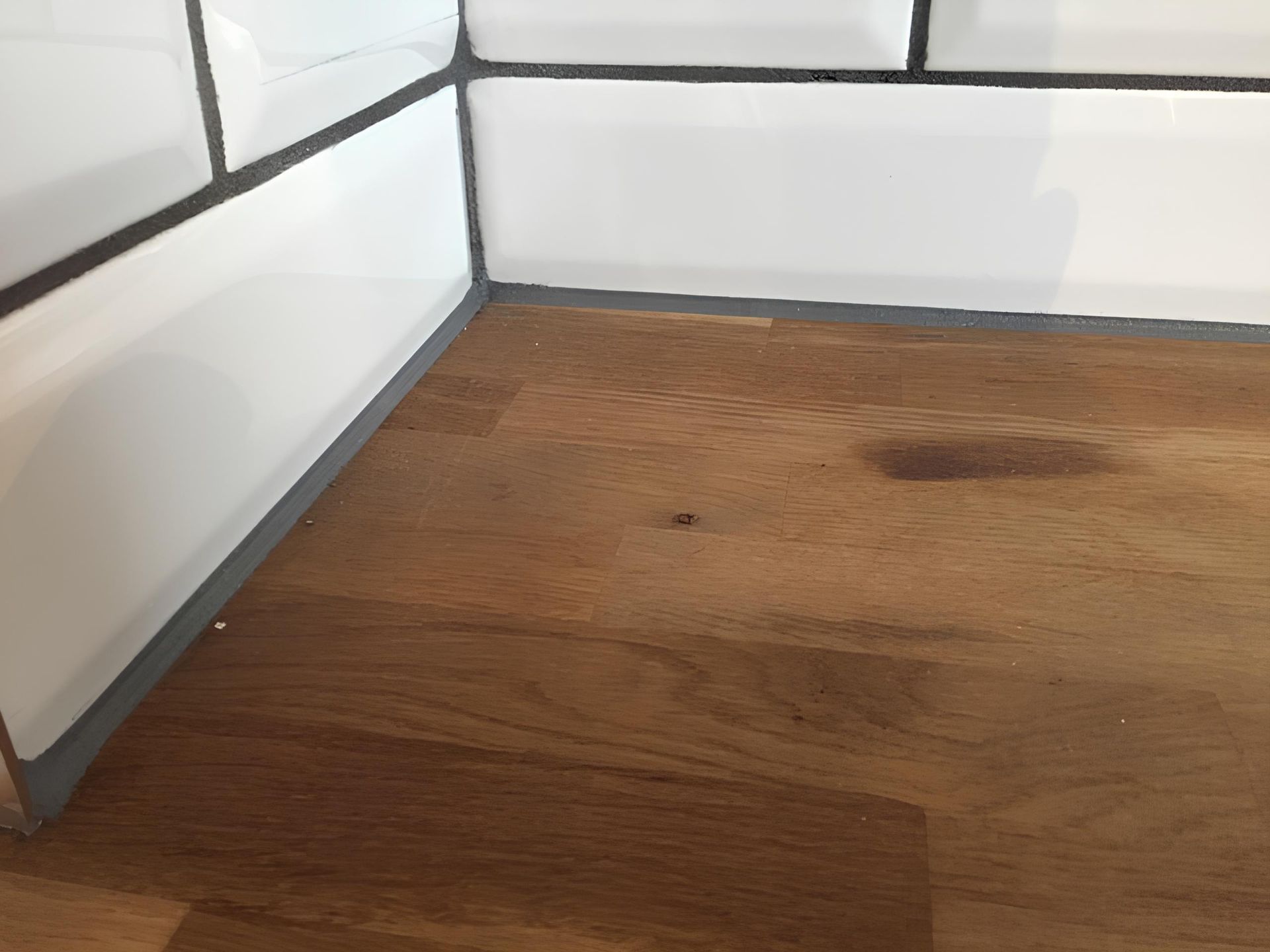 Wooden countertop with white tiled backsplash and gray sealant.