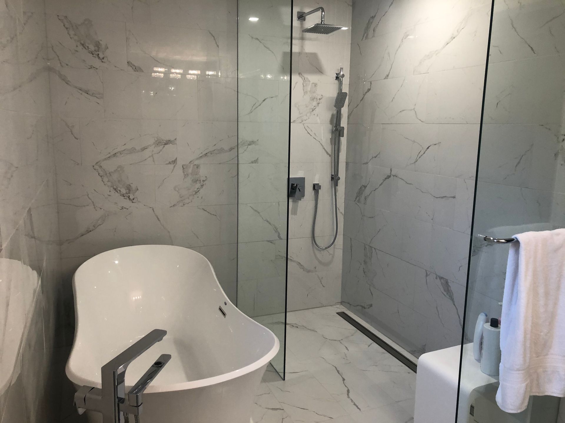 Modern bathroom with white marble tile, glass shower, and freestanding bathtub.