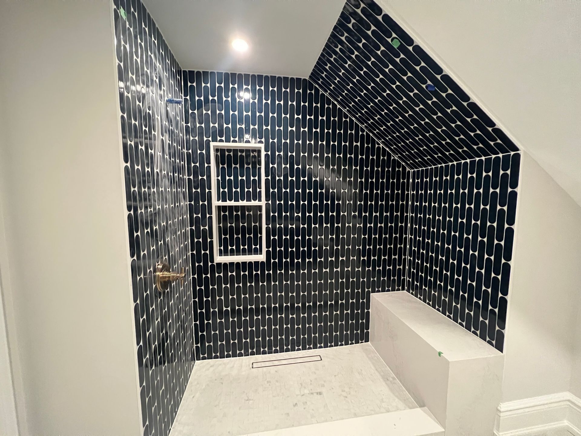 Shower with black and white tiled walls, built-in bench, and recessed storage niche.